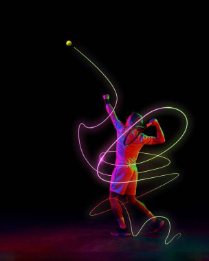 Odaklanmış bir adam, hareket halindeki bir tenisçi, neon yeşil ve pembe ışıklı raketi olan bir top, siyah arkaplana karşı hareketi vurguluyor. Spor kavramı, rekabet, turnuva, oyun.
