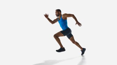 Kaslı kararlı bir adam, mavi formalı bir koşucu, kısa şortlu, beyaz stüdyo arka planında tek başına çalışıyor. Spor anlayışı, rekabet, dayanıklılık, atletizm. Boşluğu kopyala