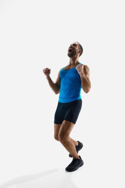 Kaslı bir adam, profesyonel bir koşucu, zaferi kutluyor, beyaz stüdyo arka planında yalnız başına elini kaldırıyor. Spor anlayışı, rekabet, dayanıklılık, atletizm, spor yaşam tarzı. Boşluğu kopyala