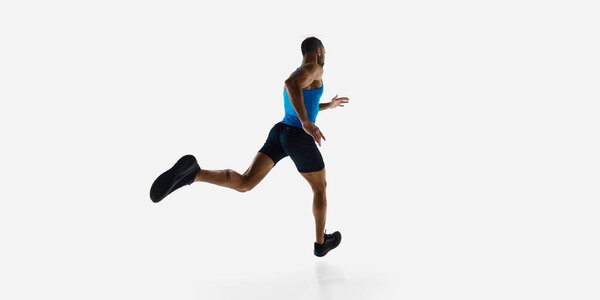 Низкий угол обзора молодого спортсмена, захваченный в середине спринта, накладывает ограничения на белый студийный фон. Вид сзади. Концепция спорта, соревнования, выносливость, легкая атлетика, спортивный образ жизни. Копирование пространства