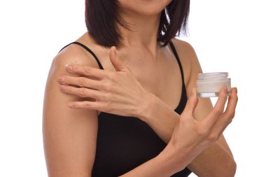 Siyah bluzlu bir kadının krema kavanozunu tutarken ve vücuduna nemlendirici krem sürerken, omuzlarına. Susuzluk ve gençleşme. Cilt bakımı kavramı, yaşlanma karşıtı tedavi, kozmetoloji