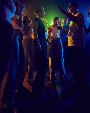 Bir grup genç, neon ışıklı odada eğlenen arkadaşlar, birlikte eğleniyorlar. Renkli ışıklar ve neşeli titreşimler gençlik kültürünün enerjisini yansıtır. Kutlama, tatil, parti kavramı