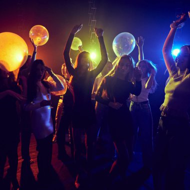 Dinamik ve şenlikli bir partide bir grup genç arkadaş birlikte doğum günü veya bayramı kutluyorlar neon ışıklarının altında neşeyle dans ediyorlar. Gençlik kültürü, parti, eğlence ve eğlence kavramı