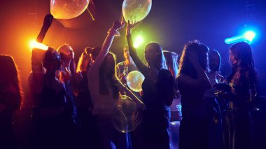 Bir grup genç, neon ışıkları altında neşeyle dans eden, gülen ve eğlenen öğrenciler. Şenlik havası. Gençlik kültürü, konser, festival kavramı