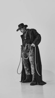 Kot pantolon, deri ceket, bot ve şapkalı, elinde kementle duran vahşi bir adamın tam boy portresi. Sakin ol. Otantik Batı estetiği. Yetenek, ele geçirme, bağımsızlık, güç sembolü