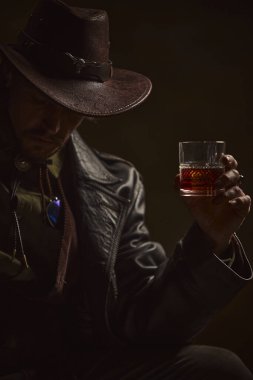 Düşünceli adam, elinde viski bardağı tutan kovboy geniş kenarlı şapkanın altında yüzü kısmen gölgelenmiş kırsal alana karşı yalnızlık ve gizem yayıyor. Batı tarihi kavramı, erkek yaşam tarzı