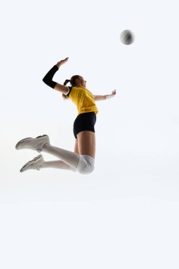 Genç sporcunun voleybol oynarken düşük açılı görüntüsü, maçın enerjisini gösteriyor, beyaz atölyenin arka planında antrenman yapıyor. Hassasiyet kavramı, meydan okuma, eylem, sağlıklı yaşam tarzı, fitness, oyun.