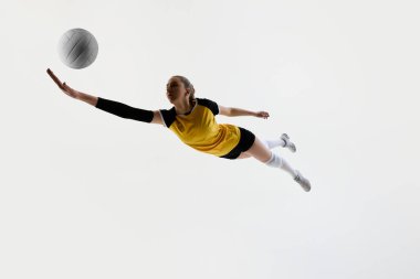 Sarı formalı genç bayan voleybol oyuncusunun düşük açılı dinamik görüntüsü ve siyah kısa eğitimli, beyaz arka planda izole bir şekilde topa vuruyor. Spor anlayışı, aktif ve sağlıklı yaşam tarzı