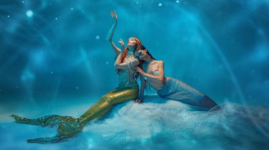 Deniz kızı kılığına girmiş, parlak kuyruklar ve inci aksesuarlar takmış narin ve zarif genç kadınlar. Mavi arka planda, yumuşak okyanus ışıltısı desenli, rüya gibi bir ifadeyle Vail 'de oturuyorlar. Fantezi kavramı