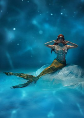 Mistik sualtı denizkızı, vücudu incilerle kaplı kızıl saçlı kadın, okyanusun derinliklerinde su gibi dalgalı arka planda oturuyor. Merak, fantezi, deniz güzelliği, peri masalı