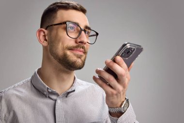 Gözlüklü, elinde akıllı telefon olan ve Grey Stüdyoları 'nın arka planına sesli mesaj kaydeden genç bir adam. Dijital yaşam tarzı, teknoloji, insan duyguları, modern iletişim kavramı.