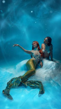 Yaz tatili. Deniz kızı gibi giyinmiş, güneş gözlüğü takmış, okyanusun derinliklerinde uzanan ve dalga desenine karşı dinlenen iki şık genç kadın. Moda, güzellik, macera kavramı