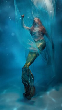 Rüyalara doğru uçuyor. Zarif genç kadın, kızıl saçlı deniz kızı şeffaf duvak ile kaplanmış, mavi okyanus benzeri arka planda dans ediyor. Rüya kavramı, fantezi, güzellik, sağlık.