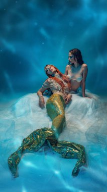 Işıldayan mavi yansımalarla çevrili, yumuşak dalgaların üzerinde dinlenen sakin denizkızları. Sakin ve rahat olduklarını ifade eden iki genç kadın. Barış kavramı, mitoloji, fantezi ve sualtı güzelliği..