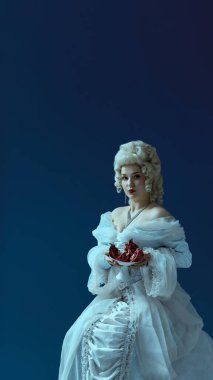 Kraliyet zevki. Klasik elbise giymiş genç düşes mavi arka planda nar yarımlı tabak taşıyor. Klasik lüks ve sembolik meyvenin birleşimi, güzellik, gizem, tarihi portre tarzı.