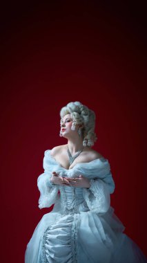 Tarihi elbise giymiş bir kadın ellerini göğsüne koyup kırmızı arka planda duygularını dışa vurarak yukarı bakıyor. Tarihsel portre kavramı, ortaçağ dönemi, karakter.