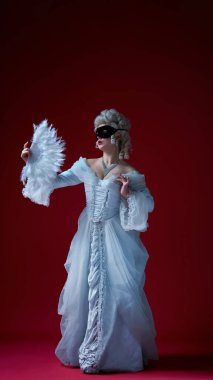 Dramatik bir açıklama. Beyaz barok cüppeli ve siyah maskeli bir kadın tüy pervanesiyle poz veriyor, sahneye benzer bir görüntü yayıyor. Tarihsel portre kavramı, Rönesans modası, yetenek, zarafet, kimlik.