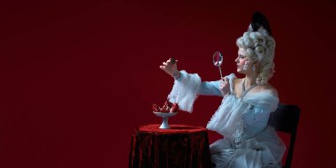 Mücevher analizi. Zarif beyaz elbiseli asil bir kadın nar yerine yakut yüzüğü incelemek için büyüteç kullanıyor. Sembolizm kavramı, değer, aşırılık eleştirisi, kraliyet ve arzunun gerçeküstü birleşimi..