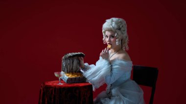 Sırları tatmak. Beyaz elbiseli, egzotik göğüsten cips yiyen barok genç bir kadının portresi, koyu kırmızı arka planda büyüleyici ve gerçeküstü bir atmosfer. Zamanın zıtlığı, mizah, moda, fantezi