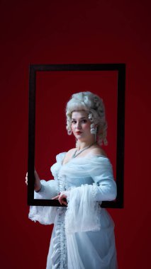 Çerçevede donmuş. Beyaz rönesans elbisesi giymiş asil bir bayan koyu kırmızı arka planda resim çerçevesi içinde poz veriyor. Dönem, güzellik, tarih, sanat, yaratıcılık, galeri, sergi kavramı karşılaştırması