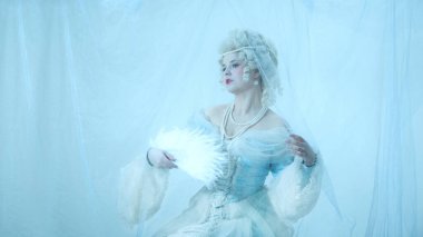 Açık mavi rokoko elbiseli, tüy yelpazeli orta çağ düşesi portresi açık mavi arka plandaki peçeye bakıyor. Dönem, güzellik, tarih, sanat, yaratıcılık kavramı karşılaştırması