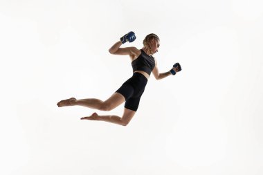 Havanın ortasında güçlü bir kadın dövüşçü, yumruklarını sıkmaya hazır, beyaz arka planda hareketsiz bir şekilde duruyor. Tayland boksu kavramı, MMA, enerji, güç, dövüş sporu, kararlılık