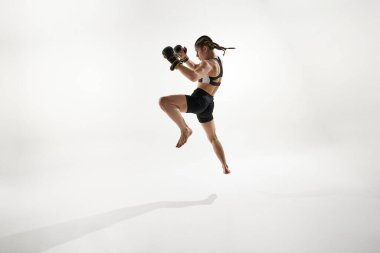 Odaklanmış siyah boks kıyafetleri içinde atlama hareketi yapıyor, beyaz arka plana karşı antrenman yapıyor. Dövüş sporu kavramı, thai boks, MMA, çeviklik, hareket, hareket, güç