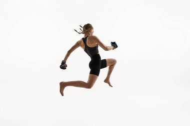 Genç bir kadının dinamik görüntüsü, Taylandlı boks sporcusu boks eldivenleriyle yüksek atlama, yoğun odaklanma ve hareketli kare. Spor anlayışı, MMA, güç, dövüş sporu, güç, dayanıklılık