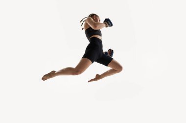 Yüksek atlamada boks eldivenleriyle yakalanan kadının düşük açılı görüntüsü, beyaz arka planda yoğun odaklanma eğitimi. Spor kavramı, thai boks, MMA, güç, hareket, kararlılık, enerji