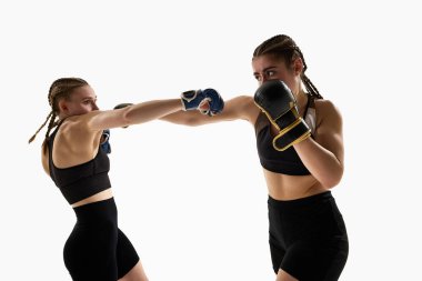 Antrenman yapan iki atletik kadın eldiven ve spor kıyafetleri giyerek yakın mesafe dövüşlerinde yumruk atıyorlar. MMA, Tayland boks, hareket, spor, güç, rekabet, eylem, enerji kavramı.