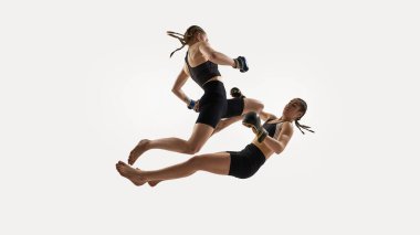 Beyaz arka planda patlayıcı dinamik hareketlerle yakalanan boks eldiveni giyen kadın sporcuların orta hava çatışması. MMA kavramı, dövüş sanatları, Tay boks, dövüş sporu, güç, çeviklik.