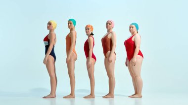 Retro mayolu ve renkli yüzme şapkalı beş genç kadın beyaz arka planda yan yana poz veriyor. Yaz konsepti, klasik, moda, mayo, güzellik, tatil, tatil, yaz havası