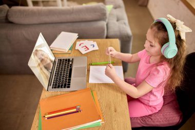 İnternetteki derse katılan genç bir kız, ekrandaki öğretmenle etkileşim halinde. Masadaki mektup kartlarını kullanarak. Evde eğitim. Çocukluk kavramı, çevrimiçi eğitim, uzaktan eğitim