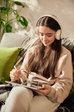 Kız kulaklıkla dijital tablette gülümsüyor ve resim çiziyor, rahat, sıcak ışıklandırılmış modern odada sanatsal aktivitelerin tadını çıkarıyor. Eğitim kavramı, evde eğitim, öğrenim, online kurslar