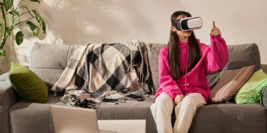 Pembe kapüşonlu kız evde sanal sınıf deneyimi yaşarken VR kulaklık kullanıyor. Gelecekçilik, modern teknolojiler. Eğitim anlayışı, evde eğitim, öğrenim