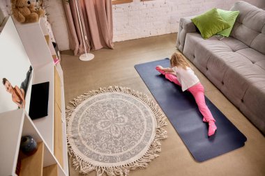 Parlak, rahat bir odada TV 'de sanal fitness dersi seyreden bir kız. Çocukluk kavramı, çevrimiçi eğitim, uzaktan eğitim, kapsamlı gelişme, spor, sağlık