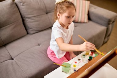 Fırça darbesine uzanan, sanatsal sürece dalmış, sanal sanat dersi sırasında hareket becerileri ve yaratıcı düşünce geliştiren bir kız. Çocukluk kavramı, çevrimiçi eğitim, uzaktan eğitim