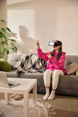 VR kulaklıklarıyla interaktif öğrenme ortamını keşfederken havada el kol hareketi yapan bir kız. Gelecekçilik, modern teknolojiler. Eğitim anlayışı, evde eğitim, öğrenim