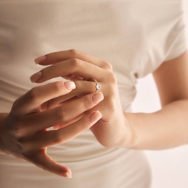 Yumuşak ışıklandırmalı nişan yüzüğüyle hassas kadın ellerine yakın çekim. Zarif beyaz elbise giyen bir kadın. Mücevher, lüks, aksesuar, düğün kavramı