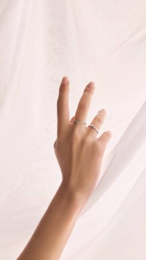 Manikürlü tırnakları olan, yumuşak, beyaz bir kumaşa iki narin yüzük takan narin kadın elinin kırpılmış görüntüsü. Mücevher, lüks, aksesuar, güzellik kavramı