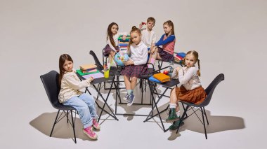 Günlük ve üniforma giymiş çocuklar sıralarda oturup kitap, küre ve kırtasiye malzemeleriyle duygularını ifade ederler. Eğitim kavramı, okul, çocuklar, ilkokul.