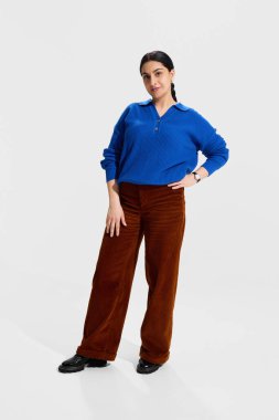 Mavi kazaklı ve kahverengi pantolonlu kendinden emin bir bayan eğitimci. Beyaz stüdyo geçmişine karşı el ele tutuşmuş, otorite yayıyor, hazır ve profesyonel bir ilişki yaşıyor. Eğitim kavramı