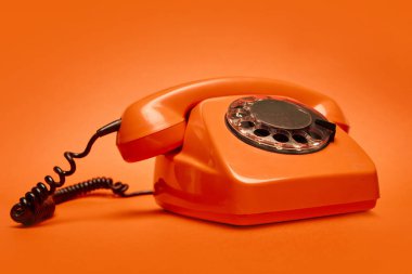 Canlı eşleşen arka planda kalın turuncu döner telefon. Klasik estetik kavramı, retro teknoloji. Poster, retro-teknoloji kampanyası, afişler için yaratıcı materyal