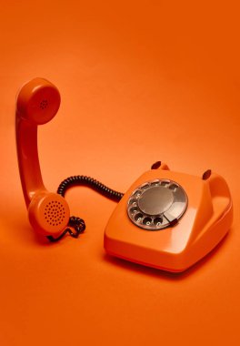 Alıcısı hafifçe kaldırılmış turuncu vintage çevirmeli telefon monokromatik turuncu zemin üzerine yerleştirilmiştir. Retro, vintage, teknoloji, pop sanatı kavramı.