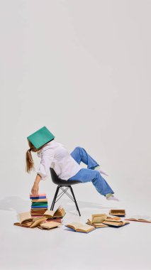 Yaşlı bir kadın, beyaz arka planda birçok renkli kitapla çevrili kitap kaplamalı bir sandalyede oturuyor. Yetişkinler için eğitim kavramı, aktif yaşlanma