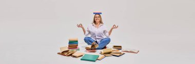 Orta yaşlı bir kadın, beyaz stüdyo arka planına karşı açık kitaplarla çevrili bir kitapla yerde bağdaş kurup meditasyon yapıyor. Yetişkinler için eğitim kavramı, aktif yaşlanma