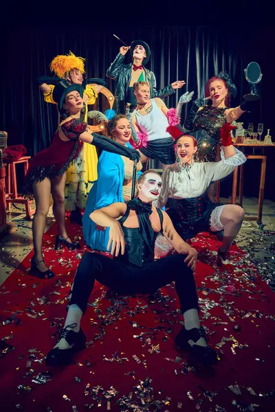 Konfeti kaplı kırmızı halıda tiyatro ifadeleri ve klasik kostümlerle dramatik poz veren bir grup kabare sanatçısı. Kabare, gösteri, sirk, retro, vintage, performans konsepti.