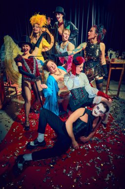 Kabare kumpanyası, abartılı jestlerle sahne ışıkları altında etkileyici kostümler ve kırmızı halıyla gülüyor ve poz veriyor. Kabare, gösteri, sirk, retro, vintage, performans konsepti.