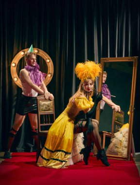 Flört eden kabare ikilisi, sarı elbiseli zarif bir kadın sigaralı ve genç bir adam, aynanın yanında klasik sandalyeli çarpıcı bir poz veriyor. Kabare kavramı, gösteri, retro, vintage, performans