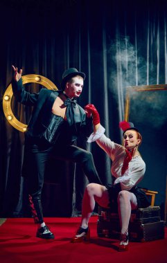 Silindir şapkalı şık kabare ikilisi sahnede sahne ışıkları altında romantik dramatik bir şekilde poz veriyor. Kabare, gösteri, sirk, retro, vintage, performans konsepti.
